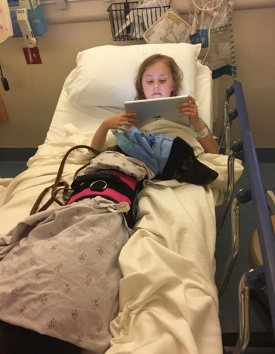 A little girl in a hospital bed with her border collie service dog.